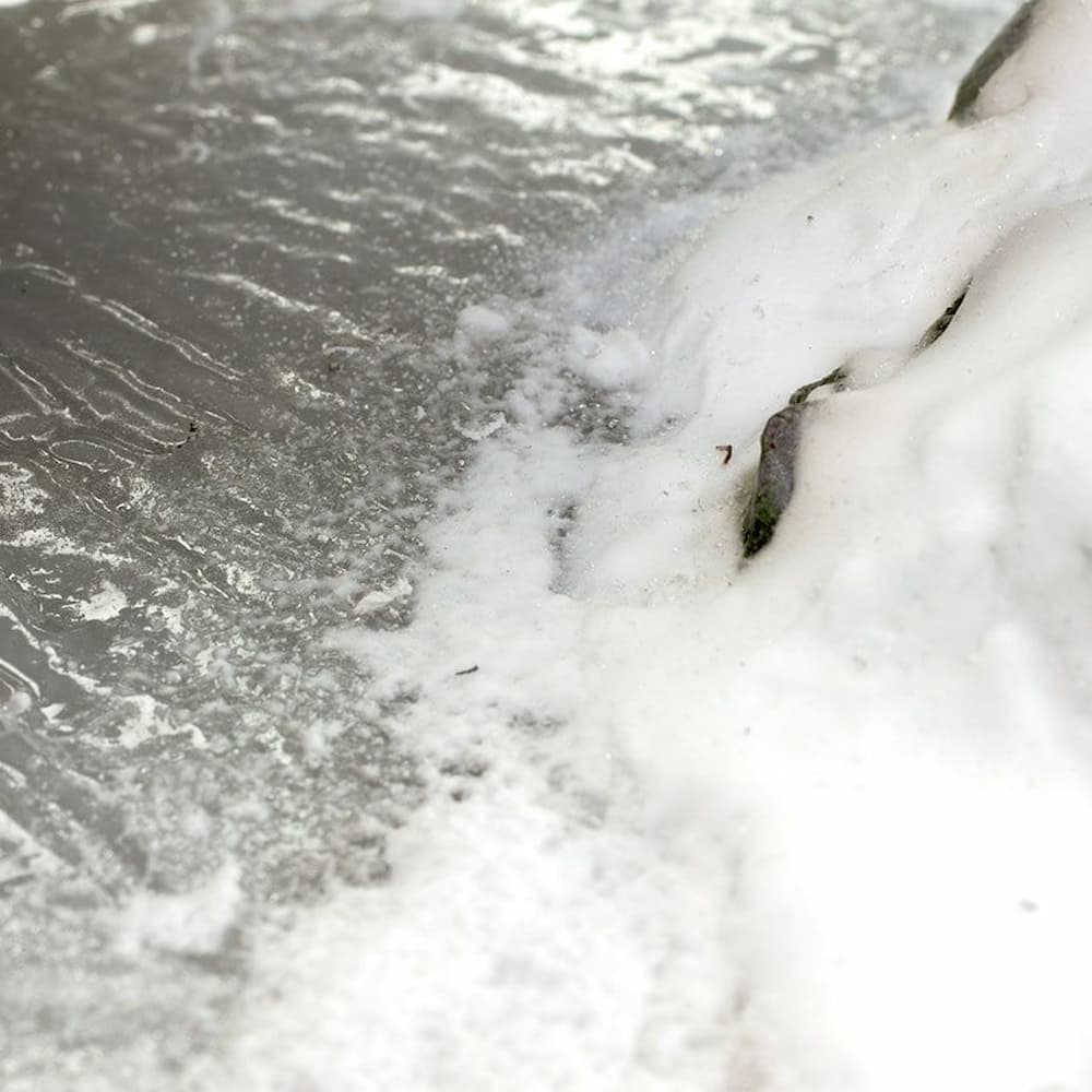 Snow-covered miniature riverbank meeting a textured gray water surface