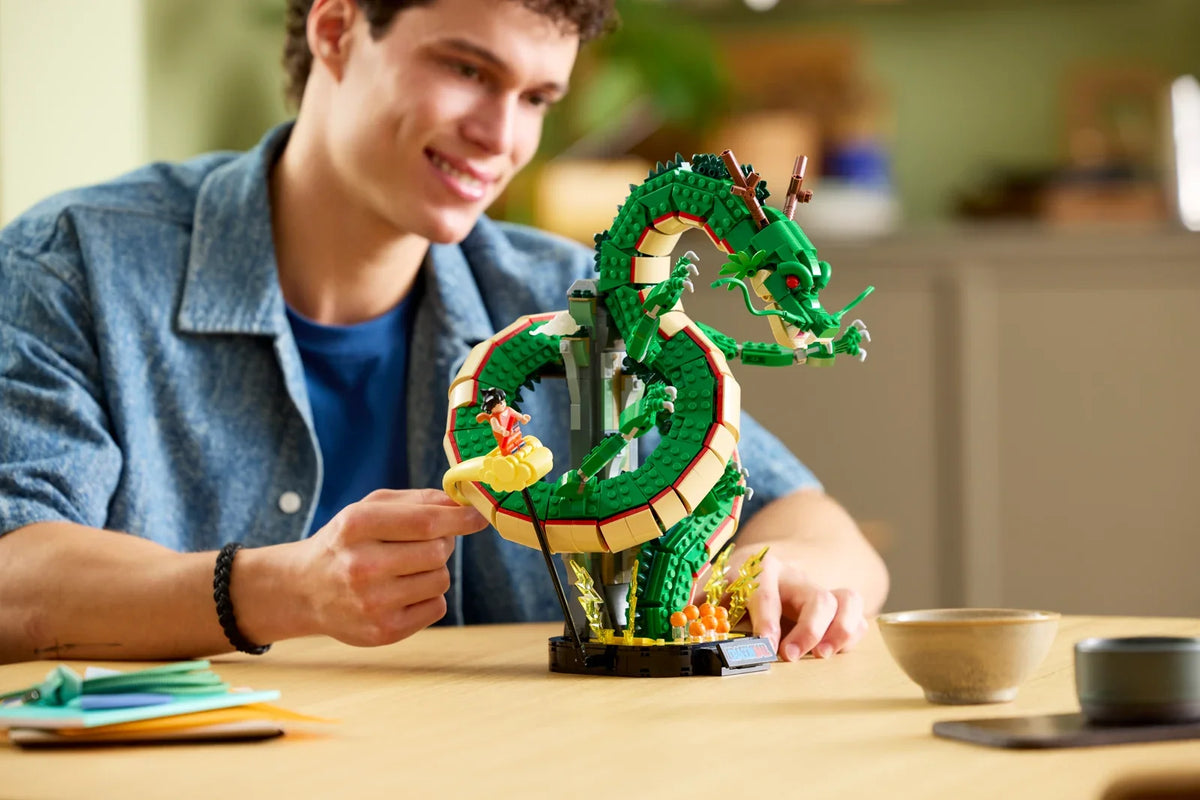 A builder adjusts Goku on Kintoun beside the completed LEGO Shenron model at a table.