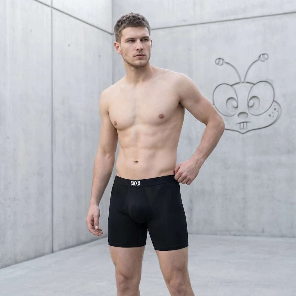 Happibee campaign model wearing black SAXX mesh boxer briefs in a concrete studio.