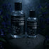 Two Sliquid Silver bottles on a dark stone display with purple flowers