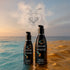 Wicked Hybrid lubricant bottles beside blue water and golden sand at sunset